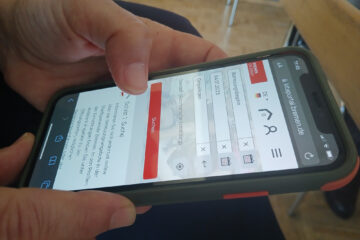 Mit beiden Händen wird ein Handy gehalten. Zu sehen ist die Startseite des Kita-Portals online.
