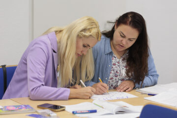 Zwei Frauen sitzen an einem Tisch und schreiben konzentriert.