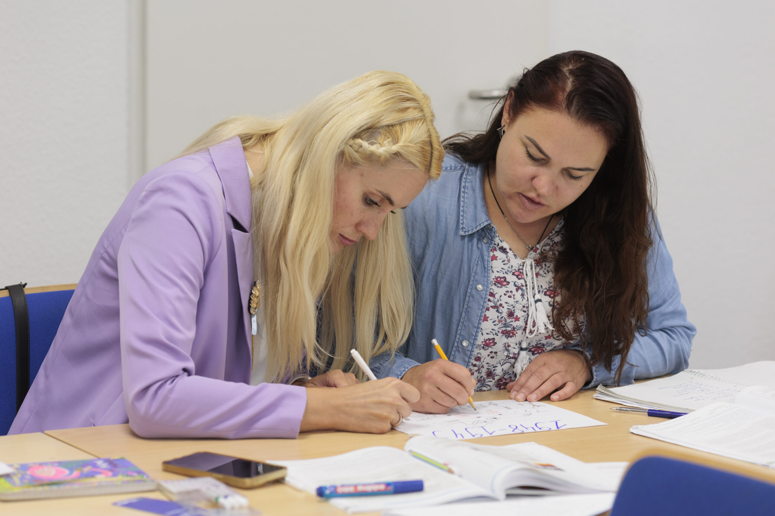 Zwei Frauen sitzen an einem Tisch und schreiben konzentriert.