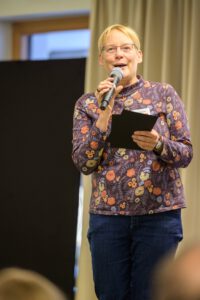 Eine Person mit blumigen Oberteil spricht über ein Mikrofon.