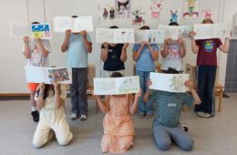 Eine Gruppe von Kindern. Jedes Kind hält sein selbst gestaltetes Buch vor das Gesicht.