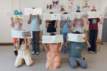 Eine Gruppe von Kindern. Jedes Kind hält sein selbst gestaltetes Buch vor das Gesicht.
