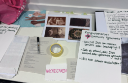 Auf einem Tisch liegen alte Fotos, Notizen, Stift und Klebeband, die den Erarbeitungsprozess zeigen.