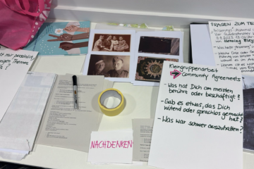 Auf einem Tisch liegen alte Fotos, Notizen, Stift und Klebeband, die den Erarbeitungsprozess zeigen.