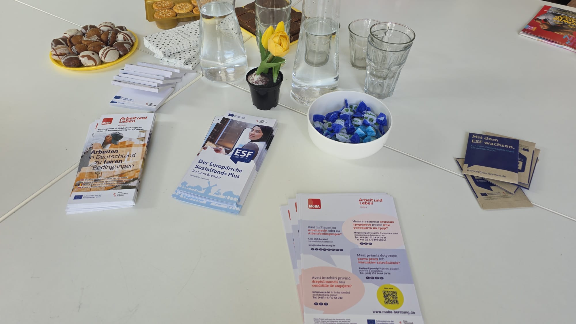 Auf einem weißen Tische liegen Info-Flyer und Knabbereien